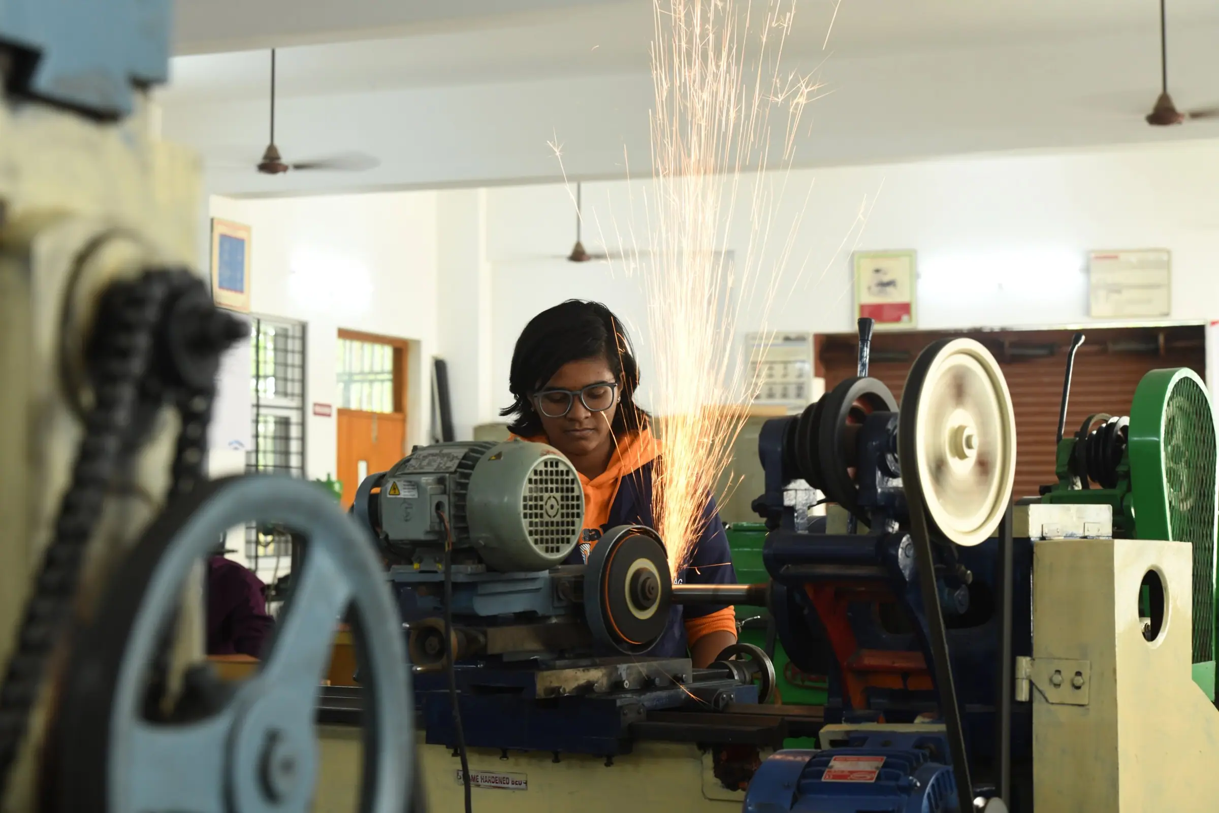 A student grinding metal in an engineering workshop, sparks flying
